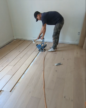Professional installer laying down hardwood planks, showcasing the labor involved